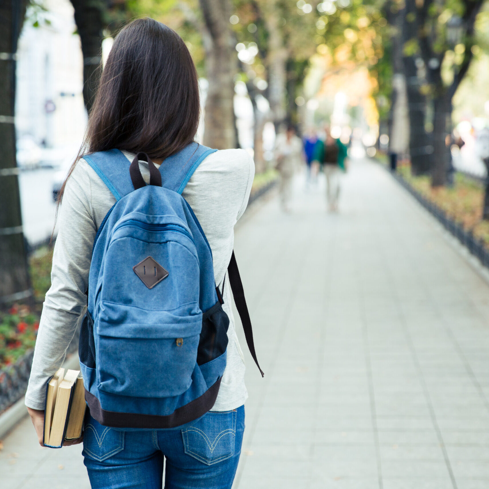 Back view portrait of a female student walking in the city park outdoors